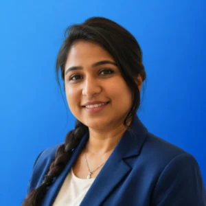 Humera Khanum Smiling woman in a blue blazer against a blue background, looking at the camera.