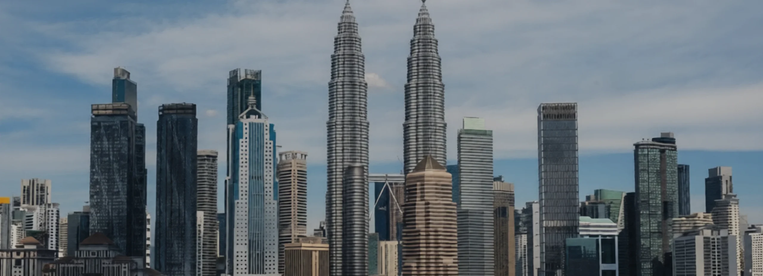 Kuala Lumpur skyline with the Petronas Twin Towers among glass skyscrapers under a blue sky,