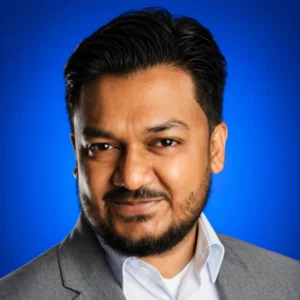 Close-up portrait of a man in a gray business suit smiling against a blue studio backdrop.