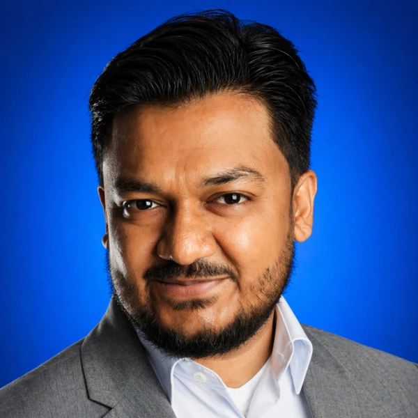 Close-up portrait of a man in a gray business suit smiling against a blue studio backdrop.