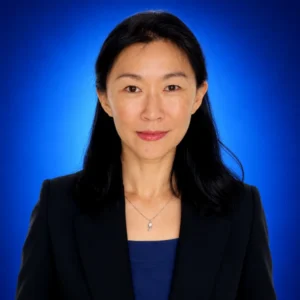 Professional portrait of a woman with dark hair in a navy blazer against a blue backdrop.