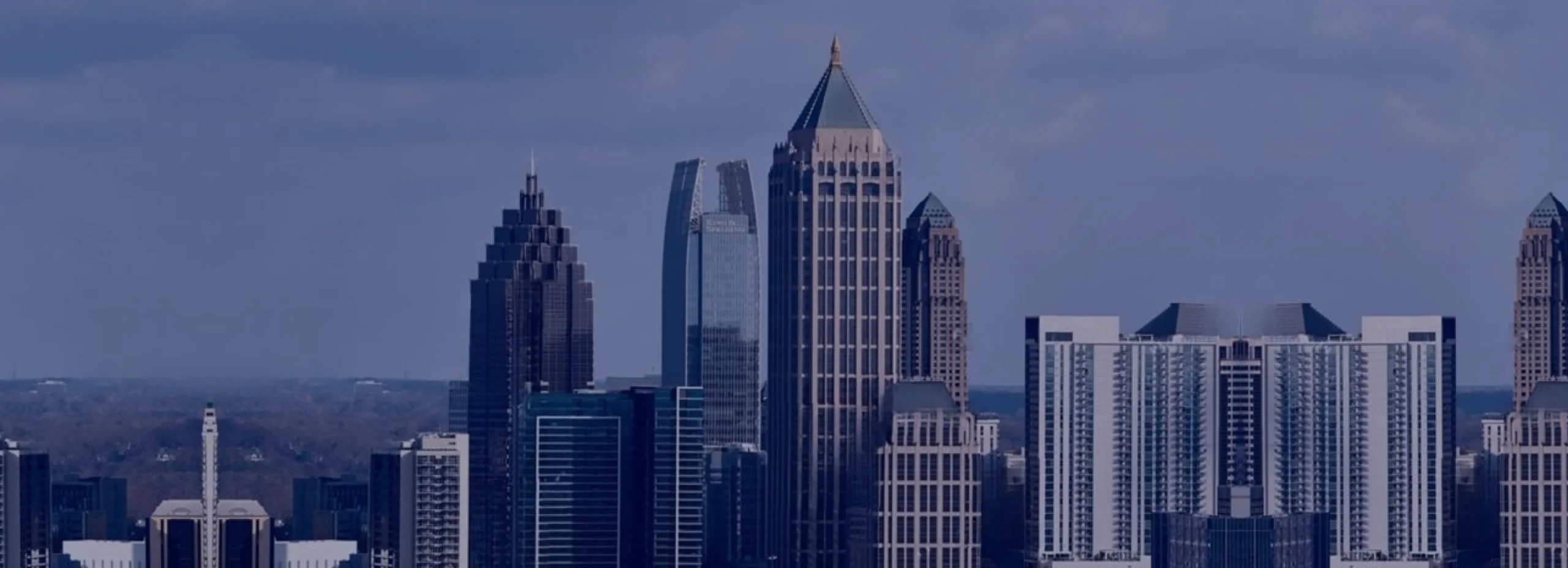 Skyline of a modern city with numerous high-rise buildings against a cloudy sky.
