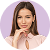 Portrait of a smiling woman with long dark hair, wearing a light-colored top, against a lavender background.