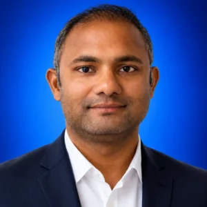 Professional headshot: man in a navy blazer and white shirt against a blue studio background.
