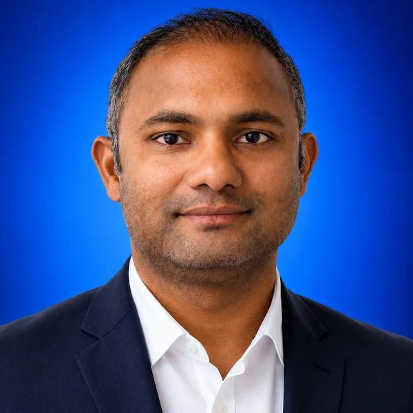 Professional headshot: man in a navy blazer and white shirt against a blue studio background.