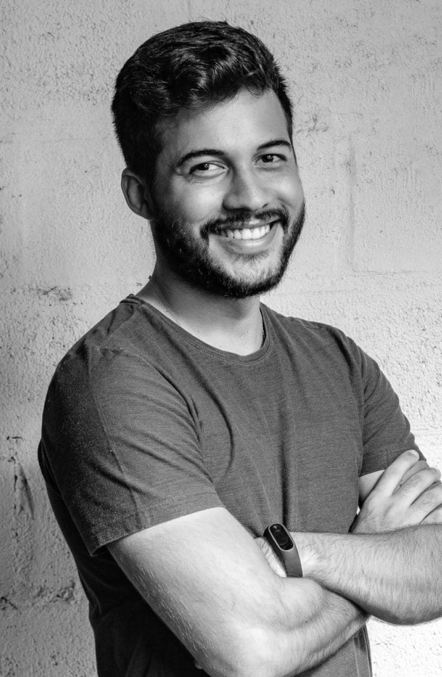 Smiling man with arms crossed, wearing a t-shirt, posed against a textured wall (black-and-white portrait).