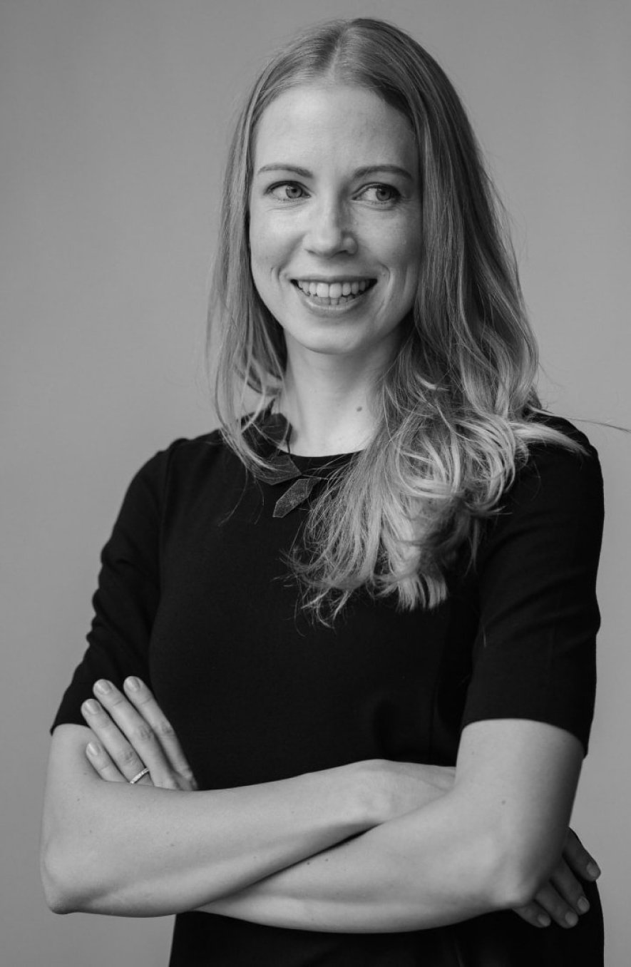 Professional portrait of a smiling woman with long hair, arms folded in a studio setting.