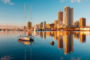 Sailboat on calm harbor with a city skyline bathed in warm sunlight reflected on the water