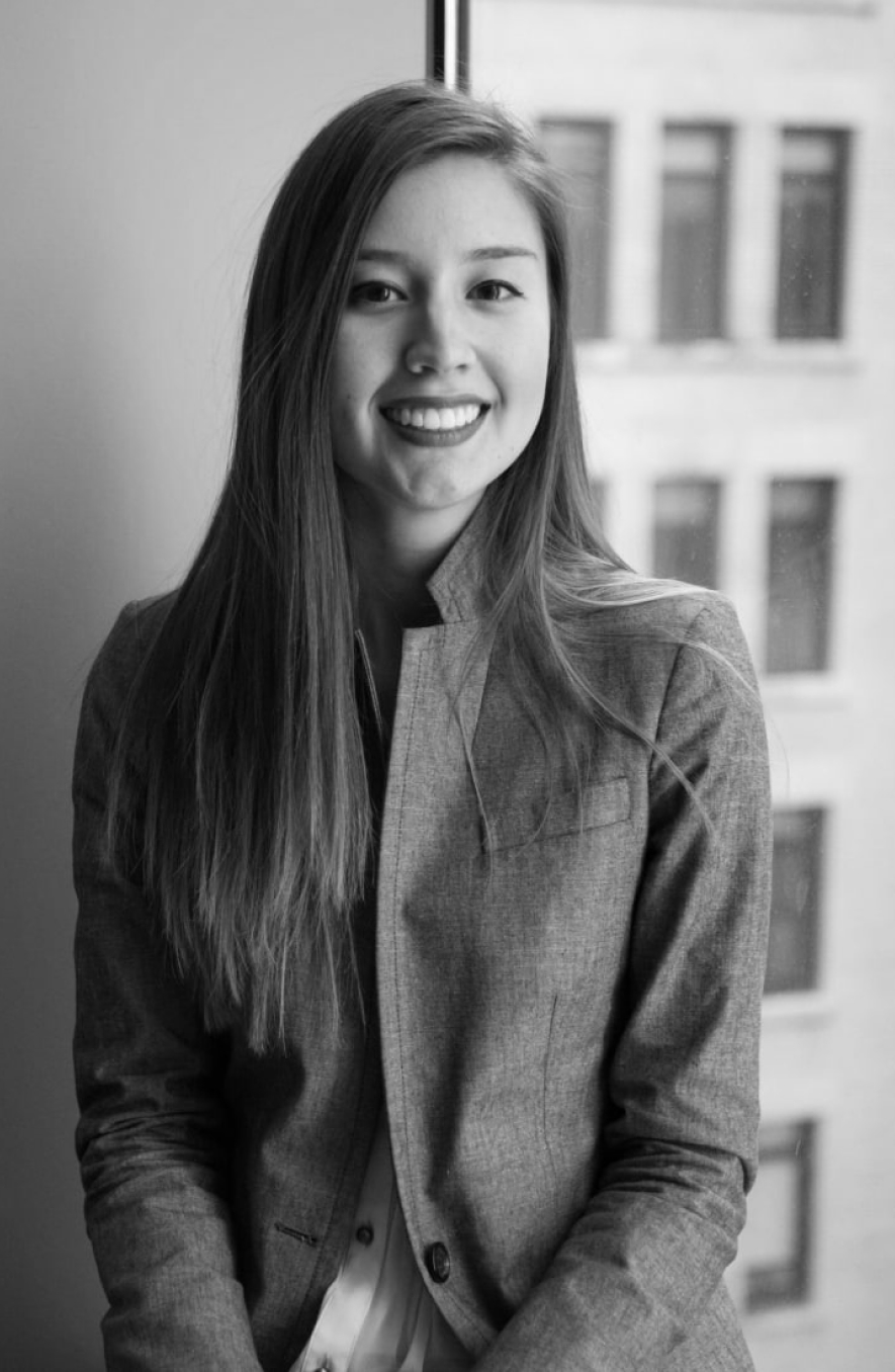Smiling woman in a blazer standing near a window in an office setting (professional portrait).