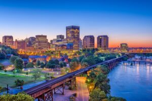 Aerial view of a downtown skyline at blue hour with a river, bridges, and illuminated buildings.