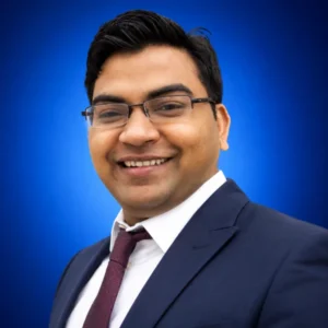 Professional headshot of a man in a navy suit, white shirt, and maroon tie, smiling against a blue gradient background.