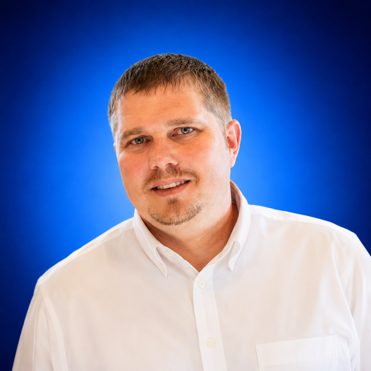 Head-and-shoulders portrait of a smiling man in a white button-down shirt against a blue gradient backdrop.