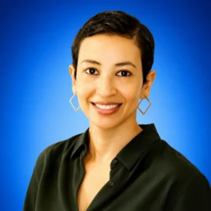 Smiling woman with short dark hair in a dark green blouse against a blue gradient background.