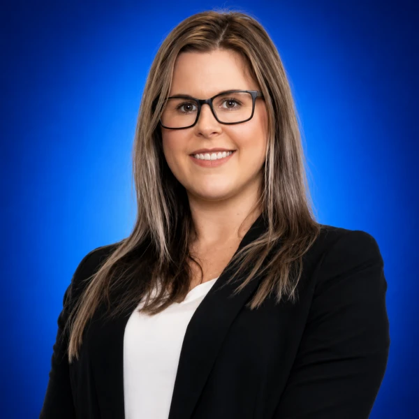 Professional headshot of a smiling woman with glasses in a black blazer and white top against a blue background.