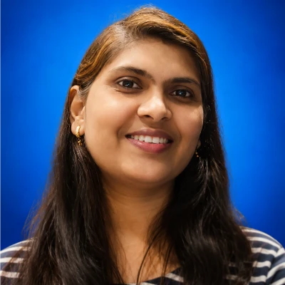 Smiling woman with long dark hair wearing a striped shirt, posed against a solid blue background.