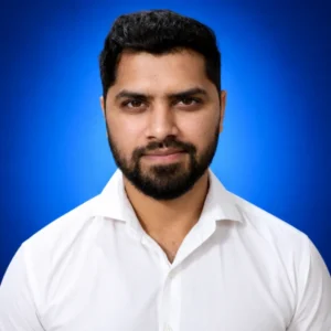 Professional headshot of a man with dark hair and beard in a white shirt against a blue gradient background.