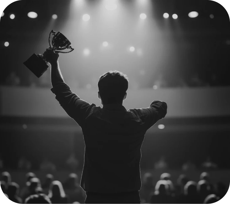 Silhouetted person on stage raises a trophy in celebration before a dim audience.