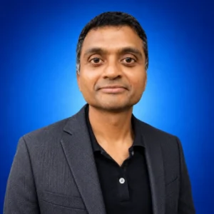 Dhiraj Peecahra Professional headshot of a man wearing a dark blazer and black shirt against a blue gradient background.