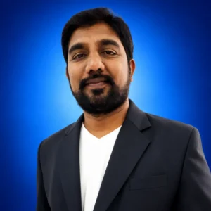Portrait of a man with a beard and mustache wearing a black blazer over a white shirt, against a blue gradient backdrop.
