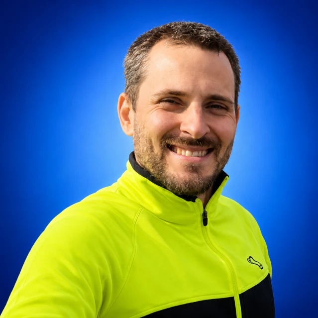 Smiling man in a bright neon yellow jacket against a blue background, close-up portrait.