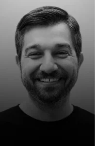 Grayscale head-and-shoulders portrait of a smiling man with short dark hair and a beard.