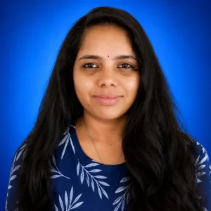 Portrait of a smiling woman with long black hair, wearing a blue patterned top, against a vivid blue background.