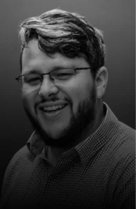 Smiling man with glasses and a beard in a checkered shirt, head and shoulders portrait in grayscale