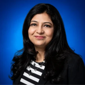 Professional headshot: smiling woman with long black hair, wearing a black blazer over a black-and-white striped top, against a blue gradient background