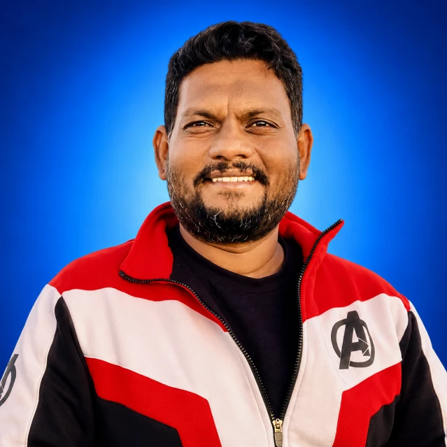 Smiling man with short dark hair and beard, wearing a red, white, and black color-block jacket with an Avengers-style logo on the chest, against a blue gradient background.
