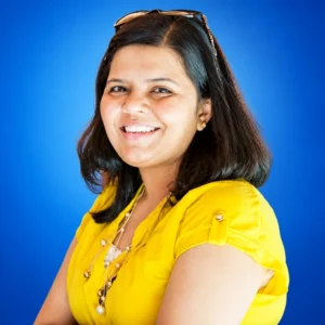 Portrait of a smiling woman with shoulder-length dark hair in a bright yellow blouse against a blue background.