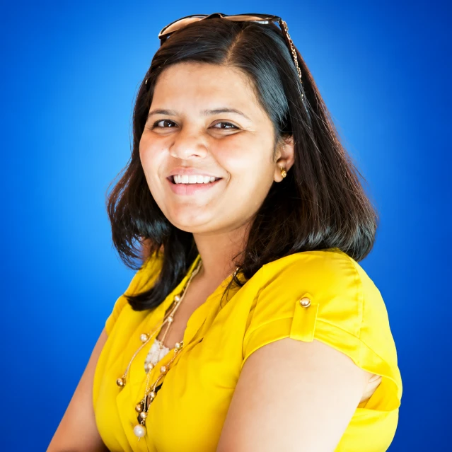 Portrait of a smiling woman with shoulder-length dark hair in a bright yellow blouse against a blue background.