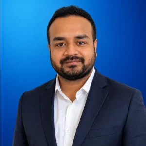 Sai Rakshit Yerram Portrait of a man in a navy suit and white shirt, against a blue gradient background with a slight smile for a professional headshot.