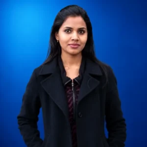 Sangeetha Thavamani Professional portrait of a woman with dark hair wearing a black coat against a blue gradient backdrop.