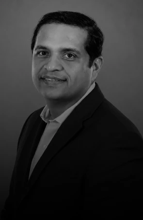 Black-and-white professional headshot of a man wearing a dark suit and light shirt, smiling softly at the camera.