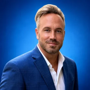 Jeff Wolf Professional head-and-shoulders portrait of a smiling man in a blue checked suit jacket and white shirt against a blue gradient background.
