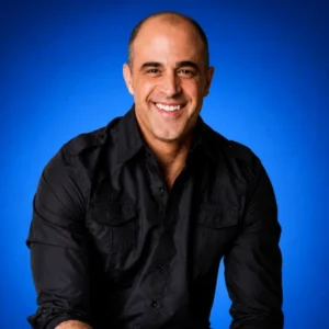 Smiling man wearing a black button-up shirt against a blue studio backdrop