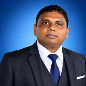 Professional head-and-shoulders portrait of a man in a dark suit, white shirt, and blue tie against a blue gradient background.