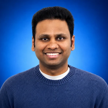 Portrait of a man with short black hair smiling, wearing a blue knit sweater against a blue gradient background.