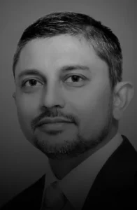 Black-and-white portrait of a man with short dark hair and a trimmed beard wearing a suit, looking at the camera.