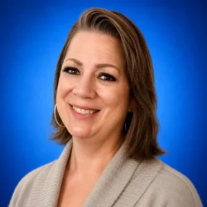 Portrait of a smiling woman with shoulder-length light brown hair in a beige cardigan against a blue background.