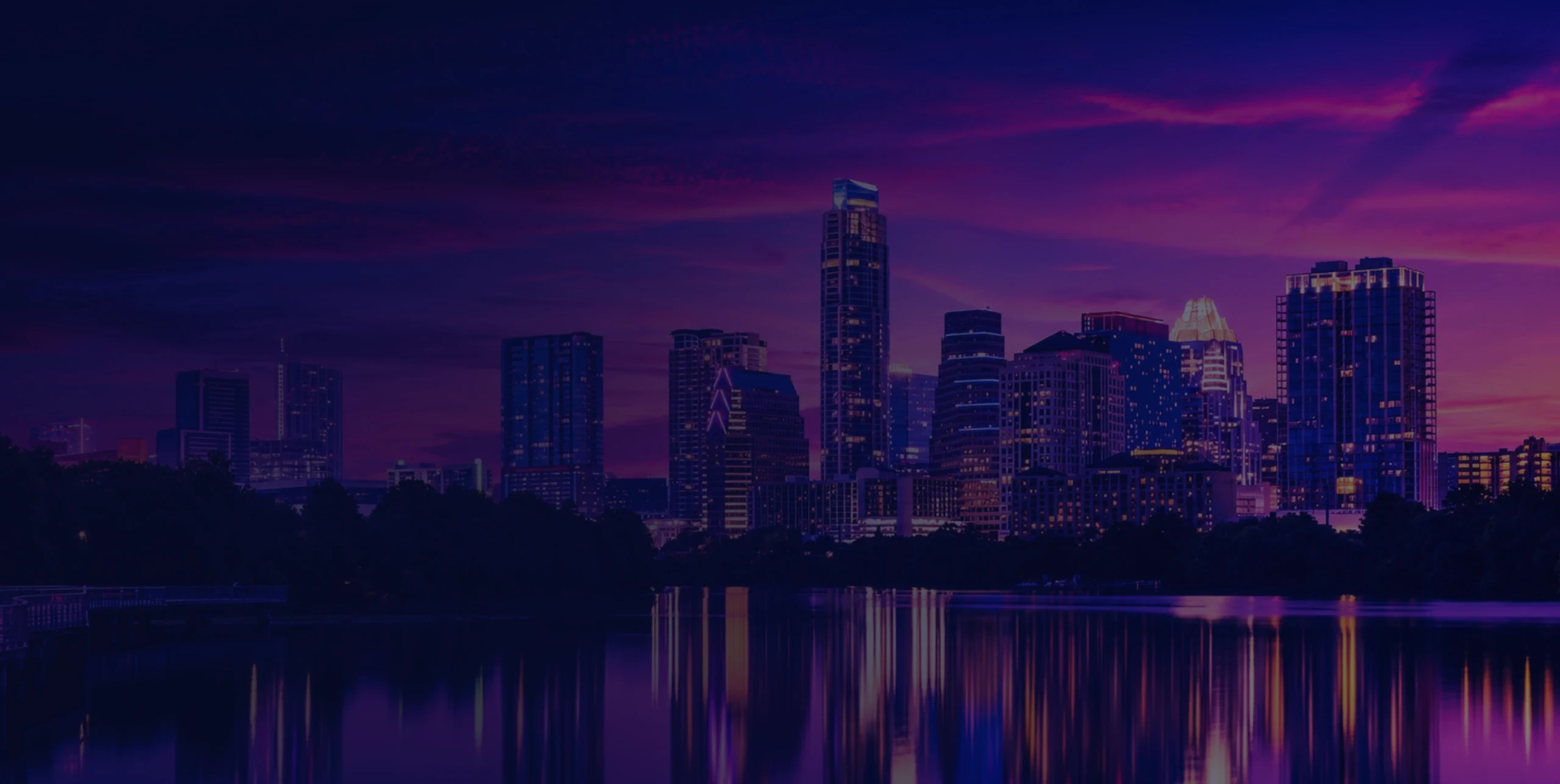 Austin skyline at dusk with tall illuminated buildings reflecting on the river, darkened so the summit details stay readable.